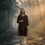 A serene devotee walking from dark forest shadows into radiant sunrise light while holding japa beads, symbolizing spiritual healing and overcoming depression through Krishna Consciousness.